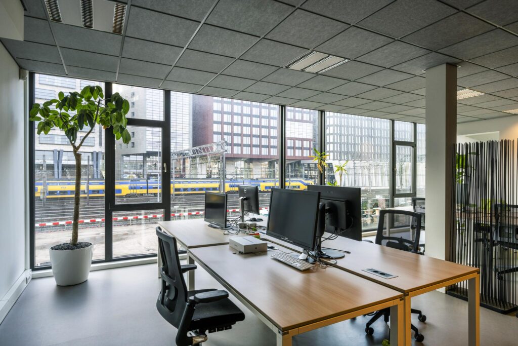 Modern kantoorinterieur aan de De Ruijterkade met uitzicht op het spoor en passerende NS-trein.